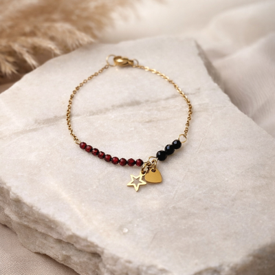 złota bransoletka z kamieniami czerwonymi i czarnymi, gwiazdką i serduszkiem - widok bizuterii leżącej na kamieniu
